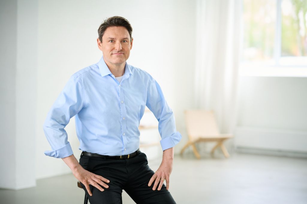 Stephan Ohlmeyer leaning in a relaxed position against a bar chair. 